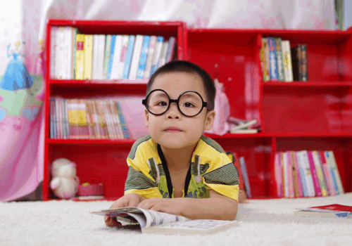 niño asiático con gafas redondas de pasta negra apoyado sobre sus codos en una mesa