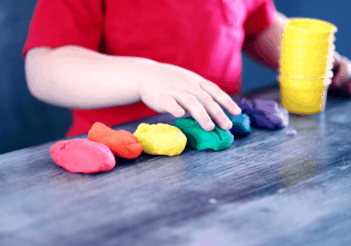 imagen de niño con camiseta roja jugando con plastilinas de colores sobre una mesa como ejercicio para integración sensorial
