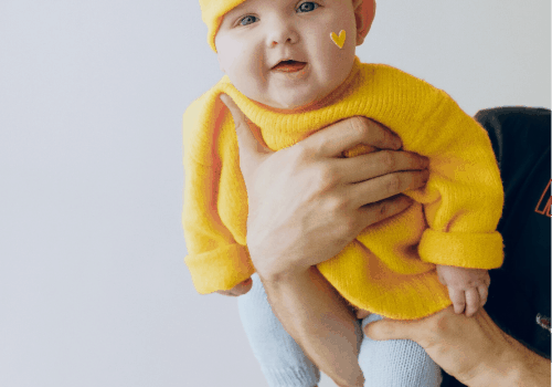 bebé con jersey amarillo cogido con manos de adulto en posición vertical