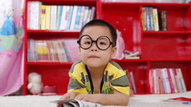 niño asiático con gafas redondas de pasta negra apoyado sobre sus codos en una mesa