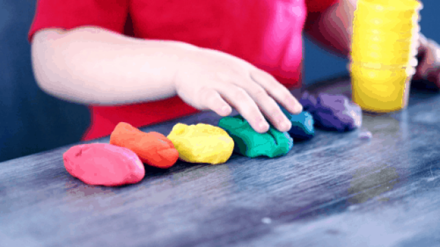 imagen de niño con camiseta roja jugando con plastilinas de colores sobre una mesa como ejercicio para integración sensorial