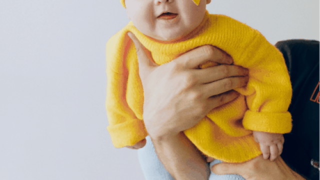 bebé con jersey amarillo cogido con manos de adulto en posición vertical